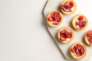 Delicious canapes with jamon, cream cheese and cherry tomatoes on light table, top view. Space for text