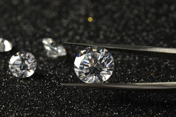 Tweezers with beautiful diamond on dark shiny background, closeup