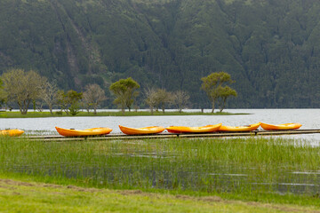 Beautiful green grass on Sete Cidades lake (Lagoa das Sete Cidades) with orange kayaks in the background. Sao Miguel, Azores