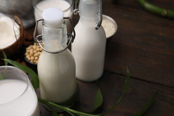 Different types of vegan milk and ingredients on wooden table, closeup