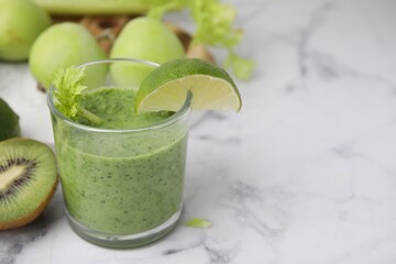 Tasty green smoothie in glass with lime and products on white marble table, closeup. Space for text