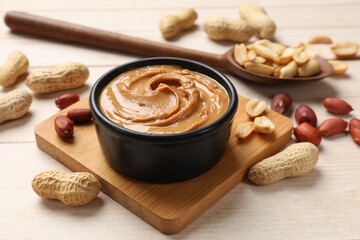 Tasty peanut butter in bowl and spoon with groundnuts on wooden table, closeup