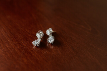 Two earrings with diamonds on them are sitting on a wooden table. The earrings are very shiny and sparkly, and they look like they are made of gold. The table is made of wood and has a warm