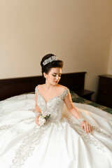 A woman in a white dress is sitting on a bed. She is holding a bouquet of flowers