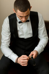 A man in a black suit and white shirt is adjusting his watch. Concept of formality and attention to...