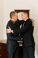 Two men in suits are hugging each other. One of them is wearing a watch. Scene is warm and friendly