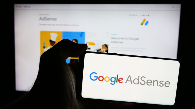 Stuttgart, Germany - 07-17-2024: Person holding mobile phone with logo of online advertising program Google AdSense in front of business web page. Focus on phone display.