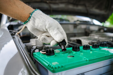 Close-up of gloved man's hand checking battery in car. Auto mechanic opens the cap to check the distilled water level in the car battery.