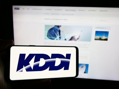 Stuttgart, Germany - 07-19-2024: Person holding mobile phone with logo of Japanese telecommunications company KDDI Corporation in front of web page. Focus on phone display.