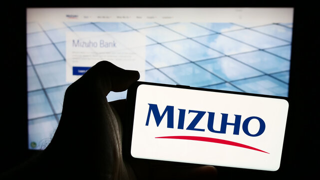 Stuttgart, Germany - 07-19-2024: Person holding cellphone with logo of Japanese banking company Mizuho Financial Group Inc. in front of business webpage. Focus on phone display.
