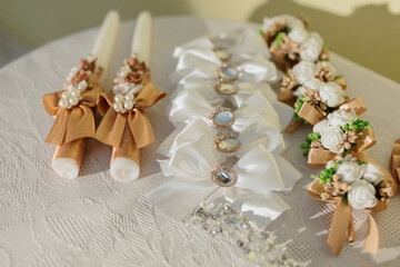 A table with candles and flowers. The candles are in different sizes and colors. The table is white and has a floral pattern