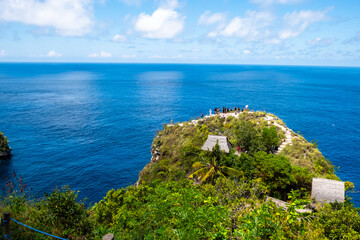Panoramic view of a cliffside with a clear ocean horizon, showcasing lush greenery and bright blue waters.
