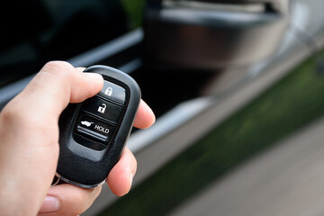 Man holding a car remote control and is pressing the car door lock button. Close up push the car door lock button on the car remote.
