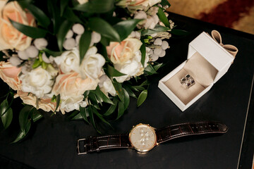 A watch is on a table next to a bouquet of flowers and a white box. The watch is a gold and black...