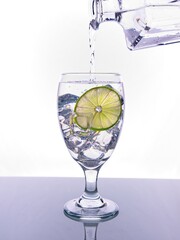 Pouring water into glass with lime slice.