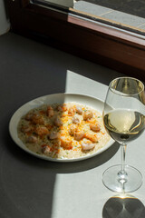 Gourmet shrimp risotto served with a glass of white wine in natural sunlight. Concept of fine dining, culinary art, and elegant meals. Vertical photo. High quality photo