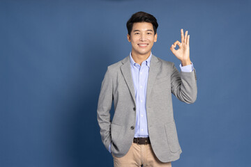 Young Asian businessman smiling and showing OK sign isolated on blue studio background