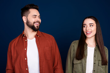 Photo of cheerful positive cute lovely couple wear stylish clothes look each other empty space isolated on dark blue color background