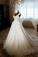A beautiful white dress with a long train is displayed in a room with a chandelier. The dress is the main focus of the image, and the room's decor adds to the elegance of the scene