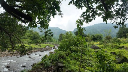 Scenic view of mountain stream cascading over rocks with green hills in the backdrop.