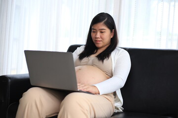 Happy pregnant woman with big tummy relax at home. Portrait of pregnant mature woman standing near the window and caresses her belly. Smiling woman expecting child and looking at camera.