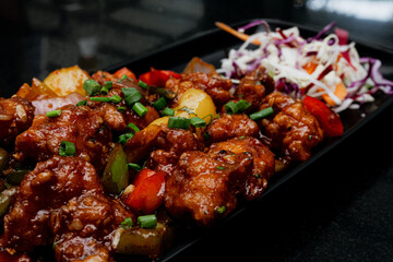 chilli chicken featuring succulent, bite-sized chicken pieces coated in a spicy, tangy sauce. Garnished with green onions and colorful bell peppers, the dish offers a vibrant and appetizing presentati