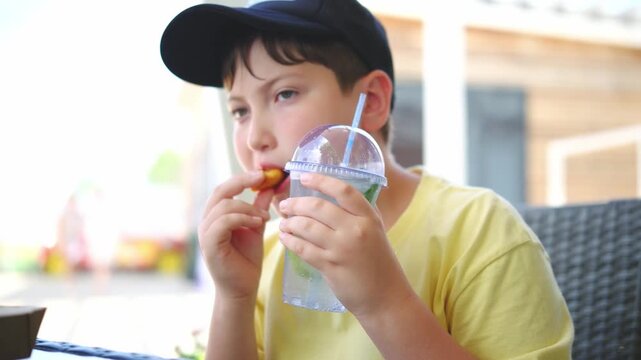 Little cute boy drinking cocktail mohito and eating nuggets outdoor on the beach.