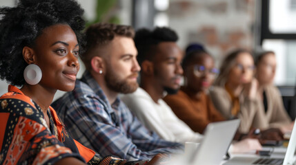 Diverse group of professionals attentively participating in a business meeting or workshop, engaging with laptops and taking notes.