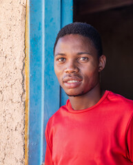 Obraz premium village african young man, with a big toothy smile, in front of the door frame of a mud house