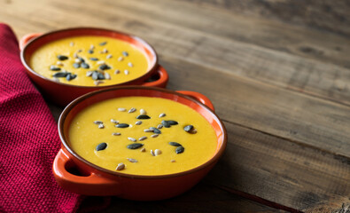 Two bowls of soup with seeds on top. The bowls are orange and are sitting on a wooden table