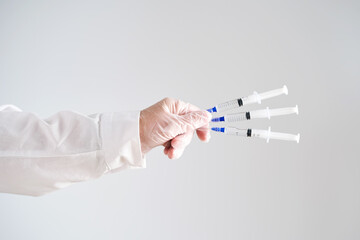 The doctor's hands in a white coat and gloves hold three syringes with medicine.