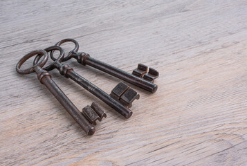 Old, rusty, iron keys on a wooden table.
