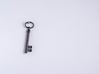 Antique rusty, iron key hanging on a nail on a white wall.
