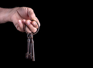 A man holds in his hand a ring with antique rusty iron keys on a black background