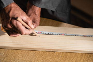Carpenter holding a measure tape on the wooden plank, makes notes, close-up. Woodwork and furniture making