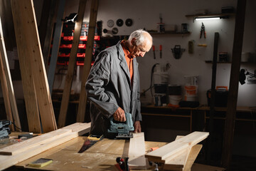 Elderly carpenter using a electric jigsaw to cut wood cuts boards in his carpentry workshop