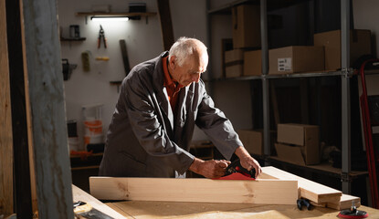mature carpenter planing plank while working in workshop enjoying favorite hobby