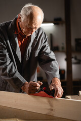 Elderly carpenter. Woodworking on a raw wood with an hand planer