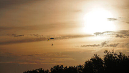 A silhouette of flying paramotor in the evening with beautiful sunset dusk sky background on the beach in Thailand.