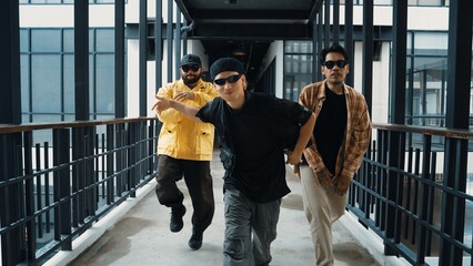 Group of smart hipster walking at modern bridge while pose at camera. Attractive handsome street dancer group looking at camera while dancing. Active, cool. Outdoor sport 2024. Hiphop.