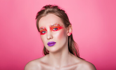 Woman with Bold Makeup on Pink Background. Young Caucasian woman with vibrant red and purple makeup, posing against a pink background. Horizontal photo. Close-up.