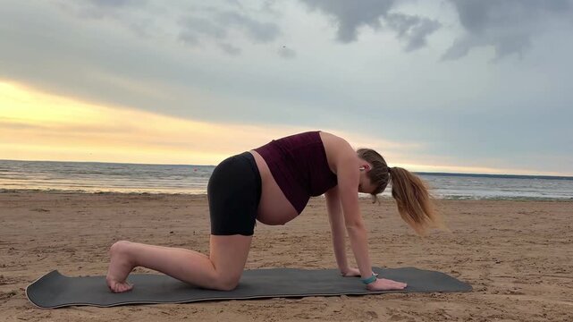 Young pregnant active woman doing exersice outdoors, stratching her body and meditate on the sea, beach at sunset in the evening