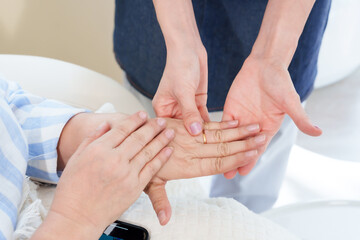 Close-up of Asian female foot spa shop owner massaging elderly Asian woman's hand. Focus on gentle, professional care in cozy nail spa setting. Emphasis on customer comfort and satisfaction.