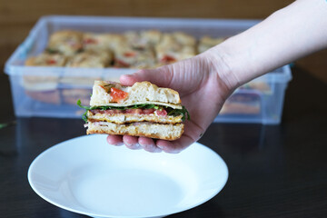 Close up a hand woman showing off a piece flatbread with filling arugula, cheese, tomatoes from the container. side view. Healthy sourdough bread