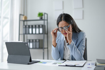 Tired businesswoman experiencing a headache, touching her temples, feeling unwell at work, suffering from dry eyes syndrome, having eyesight problems