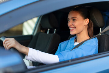 Cheerful young female doctor driving her car, smiling nurse driving home after day's work in...