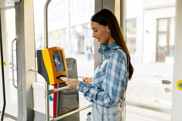 Easy payment for transportation. Happy woman passenger taking ticket in public transport tram or...
