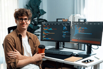 IT developer in online software development looking at camera and holding coffee cup surrounded coding pc screens, working on design new programing for latest version at modern home office. Gusher.