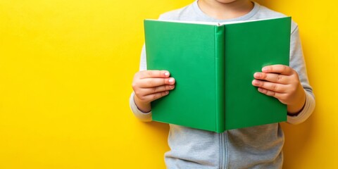A pair of hands holding a open green book set against a yellow background