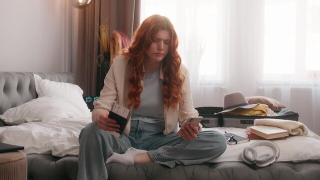 Sad frustrated dissatisfied Caucasian woman at bedroom problem looking mobile phone notification missed delay cancel flight hold passport and tickets female girl trouble trip travel journey cancelled